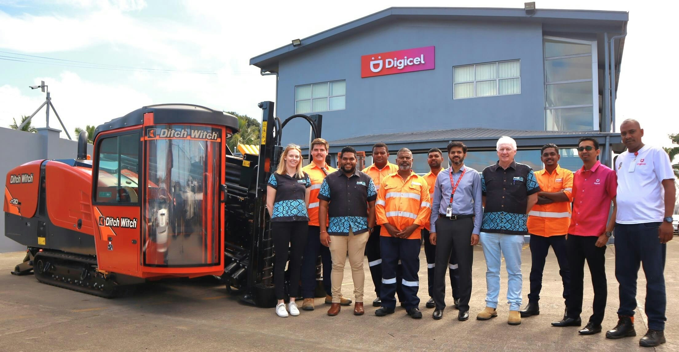 A group of Digicel staff standing next to a horizontal drilling machine